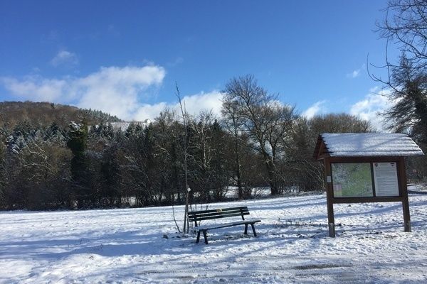 Schneelandschaft mit einer Sitzgelegenheit und einer Tafel mit einer Wanderkarte abgebildet